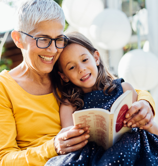 An older woman smiling and reading a story to a child who is sitting on her lap